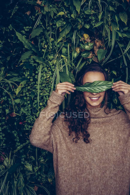 Souriante jeune femme couvrant ses yeux d'une feuille — Photo de stock