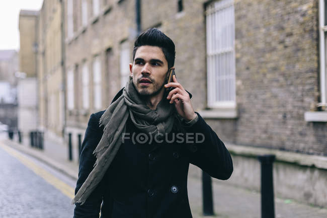 Jeune homme décontracté marchant dans la rue en utilisant un téléphone mobile — Photo de stock