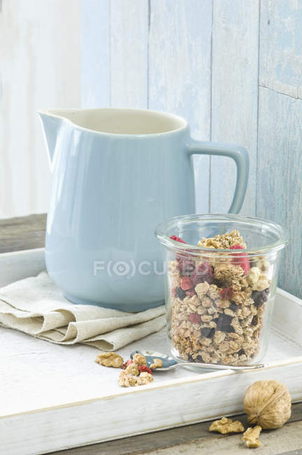 Glass of granola with walnuts, dried blueberries and raspberries and a milk jug — Stock Photo