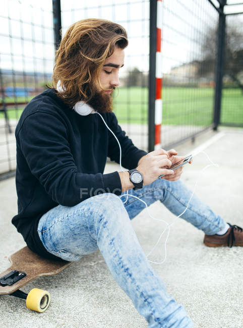 Patinador joven barbudo con smartphone y auriculares - foto de stock