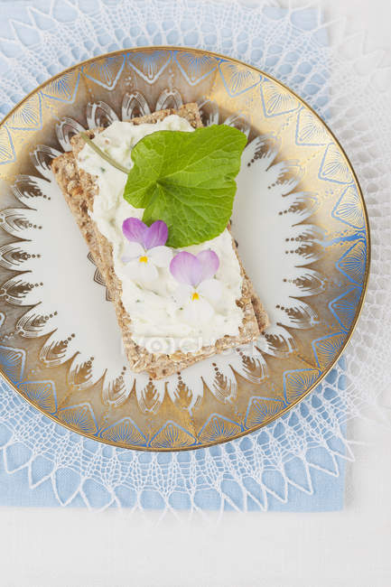 Queso crema con violeta y wasabi sobre pan crujiente, flores comestibles - foto de stock