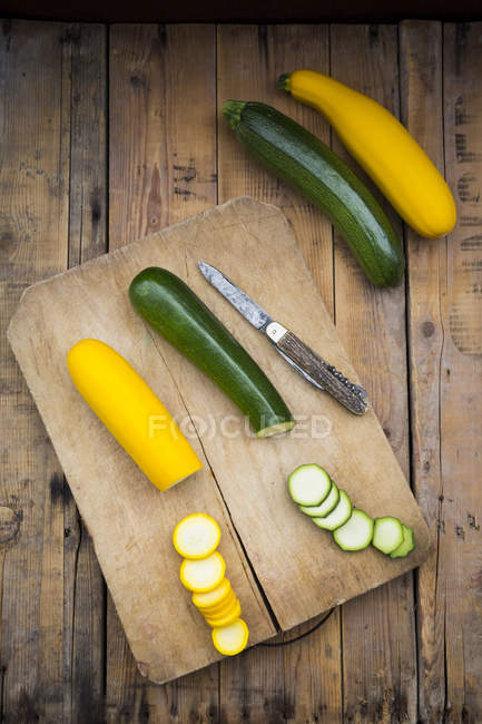 Whole and sliced yellow and green zucchini on wood with wooden board — Stock Photo