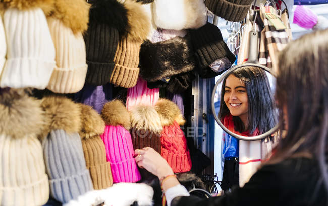 Young woman choosing wooly hat at stall — Stock Photo