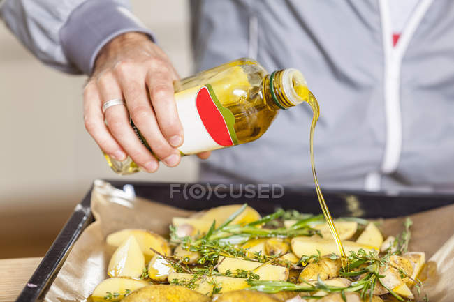 Verter aceite sobre cuñas de patata en bandeja para hornear - foto de stock