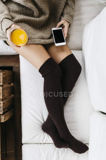 Woman relaxing with smartphone and glass of orange juice — Stock Photo