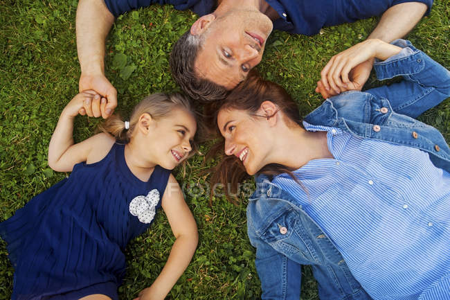 Happy family lying on grass, holding hands — Stock Photo