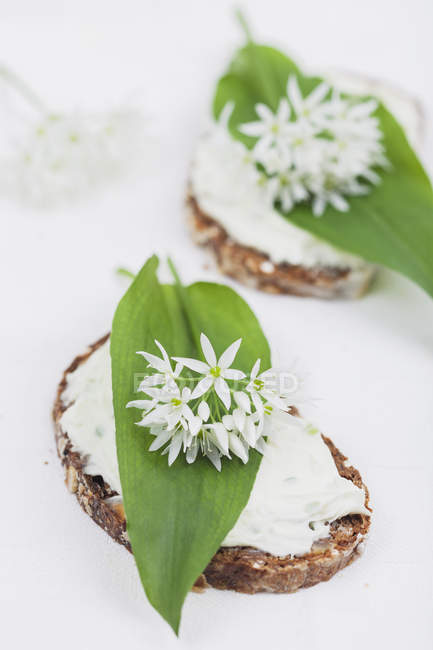 Slice of bread with cream cheese and fresh ramson, eatable blossom — Stock Photo
