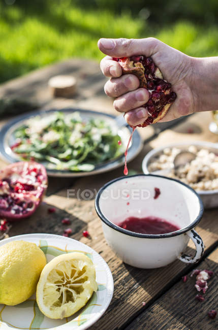 Cropped view of human hand squeezing pomegranate to bowl — Stock Photo