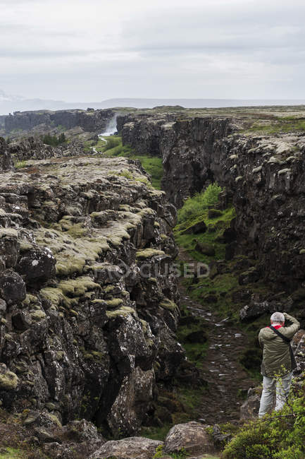 Исландия, зона разлома Тингвеллир и человек с камерой на скале — стоковое фото