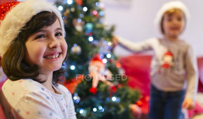 Portrait of happy girl at Christmas tree with sister on background — Stock Photo