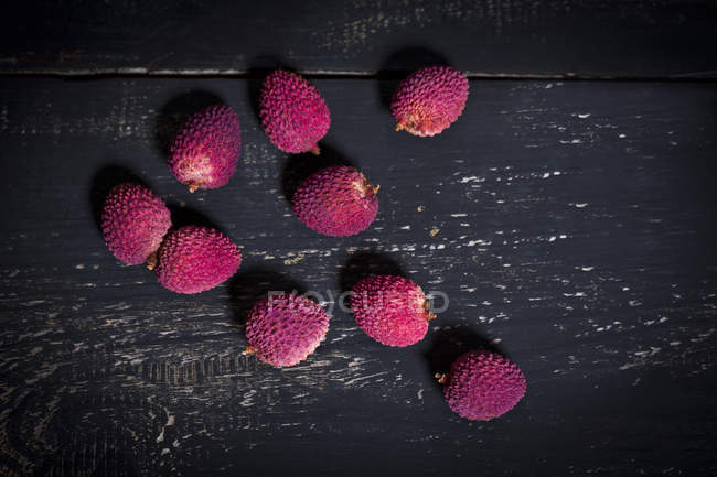 Fresh unpeeled Lychees on dark wood — Stock Photo