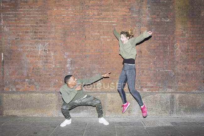 Verspieltes junges Paar springt nachts vor Ziegelmauer — Stockfoto
