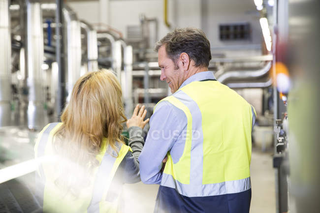 Colleagues wearing reflective vests talking in industrial plant — Stock Photo