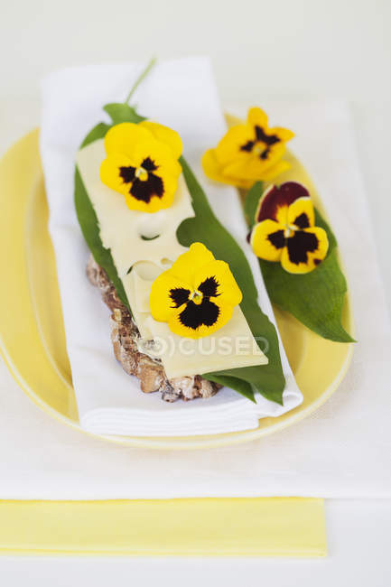 Slice of bread garnished with cheese, leaf of ramson and pansies — Stock Photo
