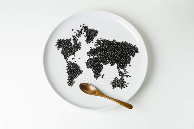 Lentilles de béluga sur plaque en forme de carte du monde avec cuillère en bois — Photo de stock