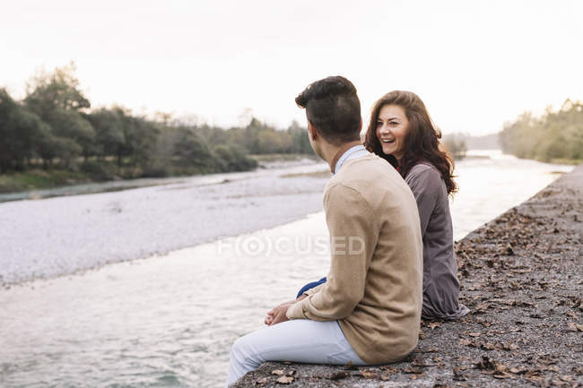 Jeune couple assis devant une rivière — Photo de stock