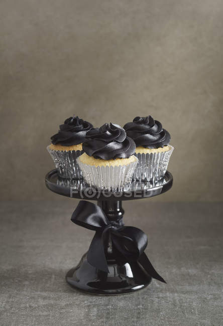 Drei Tassen Kuchen mit schwarzem Buttercreme-Belag auf einem Kuchenständer — Stockfoto