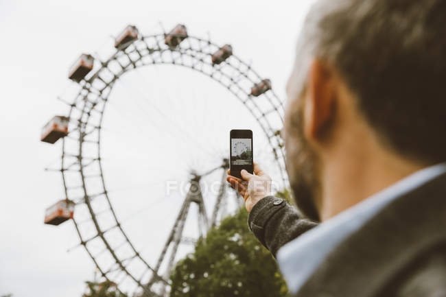 Бизнесмен фотографирует большое колесо со своим смартфоном в Пратере — стоковое фото