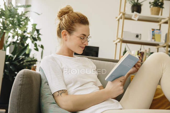 Young woman at home, looking at her book, smiling — Stock Photo