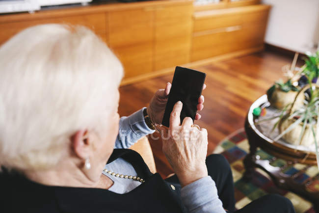 Seniorin sitzt mit Smartphone im Wohnzimmer — Stockfoto