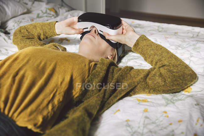 Woman wearing virtual reality glasses lying on bed — Stock Photo