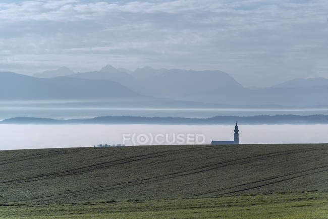Austria, Ostermiething, Church in the fog, mountains in the background — Stock Photo