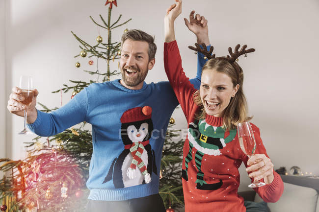Duas pessoas com camisolas de Natal feias dançando na frente da árvore de Natal — Fotografia de Stock