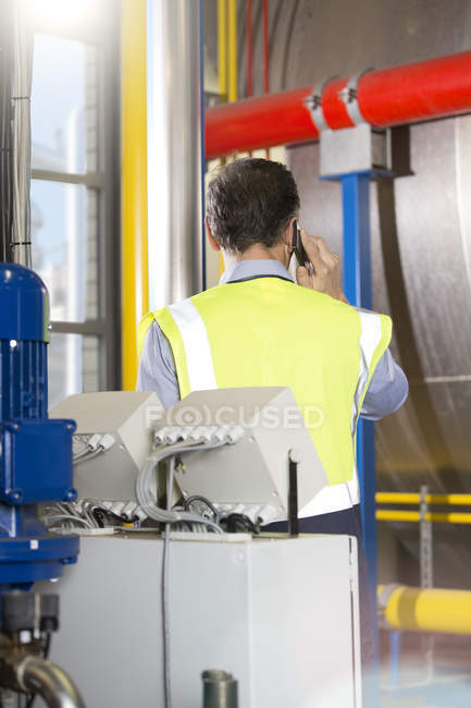 Hombre usando chaleco reflectante telefoneando en planta industrial - foto de stock