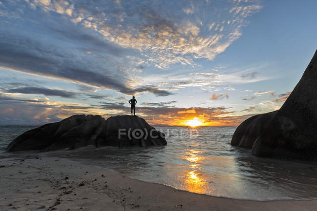 Seychelles, La Digue, praia, homem de pé sobre pedra de granito ao pôr do sol — Fotografia de Stock