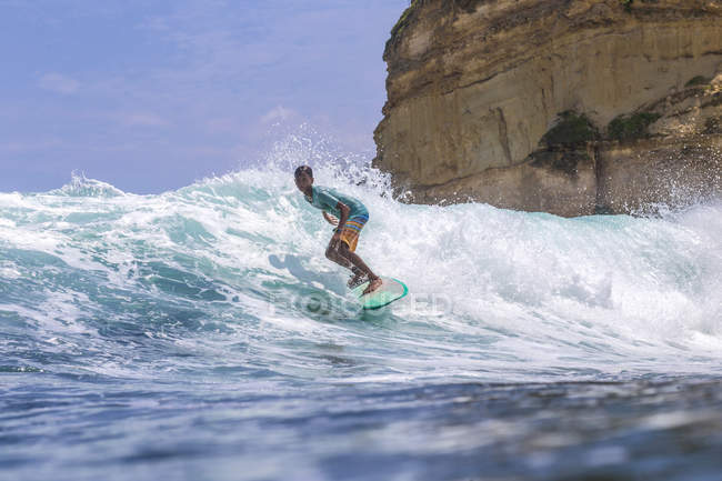Indonesia, Lombok, surfista su un'onda vicino alla roccia nell'oceano — Foto stock