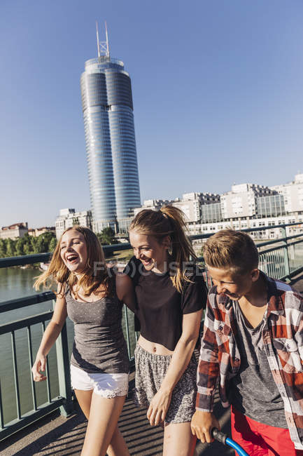 Áustria, Viena, três adolescentes felizes caminhando em uma ponte em frente à Millenium Tower — Fotografia de Stock