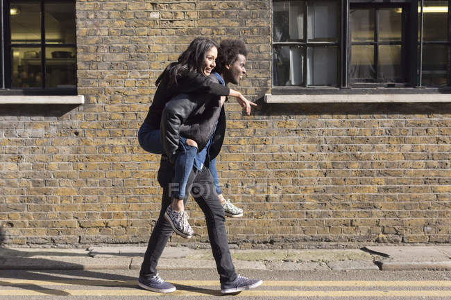 Молодой человек несет подружку на спине в кирпичном здании — стоковое фото