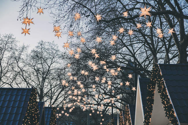 Decoration of paper stars garland lights on tree and roofs of Christmas market huts — Stock Photo