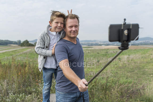 Retrato de pai e filho tirando uma foto com vara selfie na natureza — Fotografia de Stock