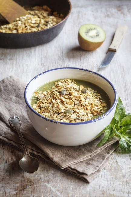 Bowl of green smoothie with mix of oatflakes and granola — Stock Photo