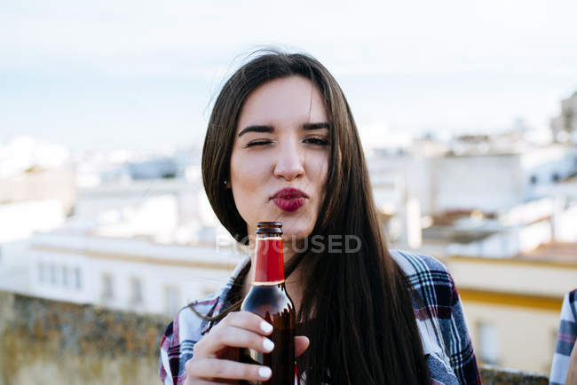 Portrait of winking young woman with beer bottle pouting mouth — Stock Photo