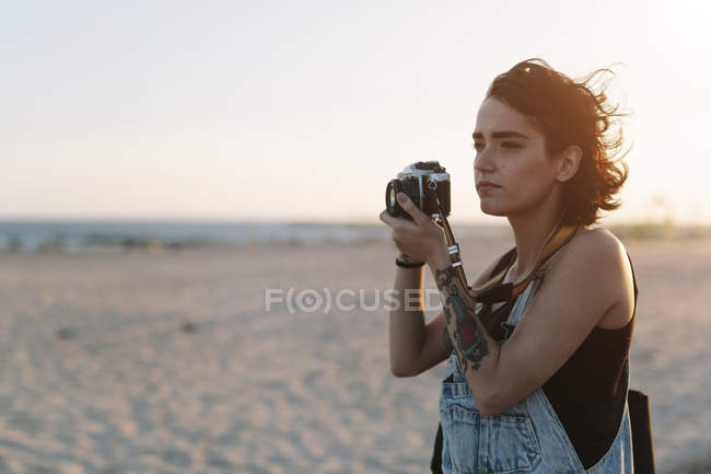 Молода жінка, беручи фотографії на пляжі на заході сонця — стокове фото