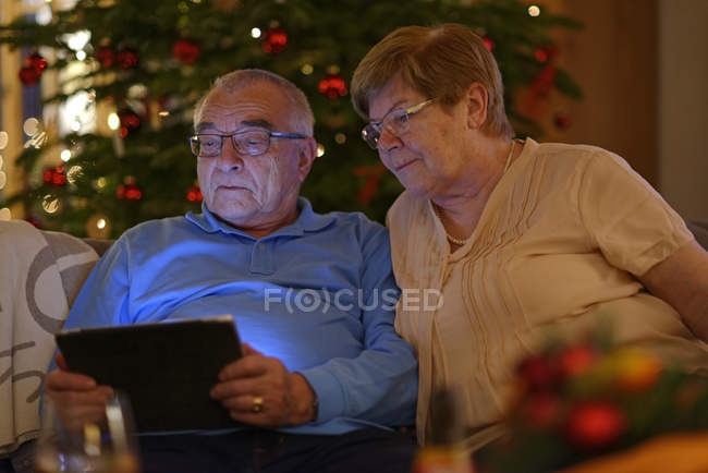 Senior couple looking at digital tablet  in front of Christmas tree — Stock Photo