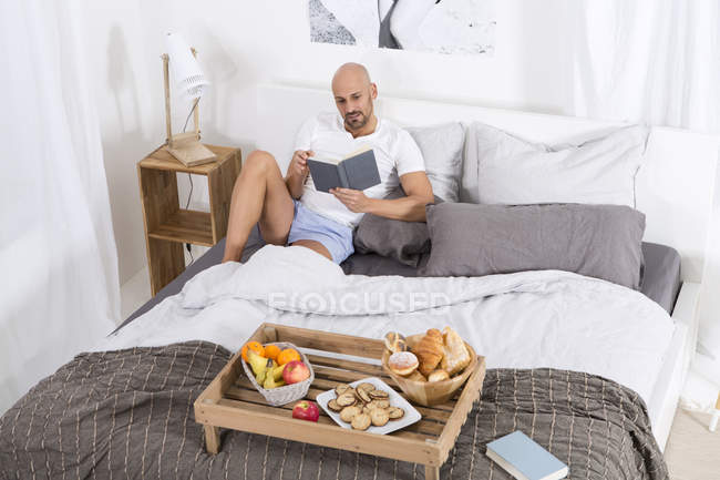 Hombre maduro con libro y desayuno en la cama - foto de stock
