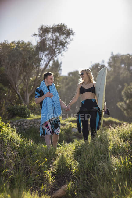 Teenage boy with down syndrome and woman hand in hand with surfboard at the coast — Stock Photo