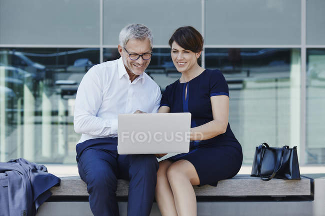 Empresario y mujer de negocios sentado en el banco de compartir portátil - foto de stock