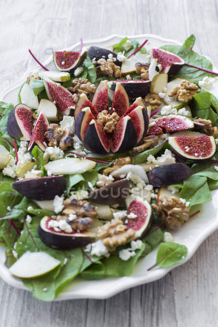 Plate of salad with mangold, feta cheese, figs, pear and walnuts on wooden surface — Stock Photo