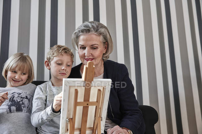 Nonna e nipote con baffi Dalì al cavalletto con ragazza guardando — Foto stock
