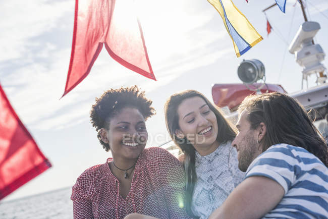 Happy friends on a boat trip sitting on deck in sunlight — Stock Photo