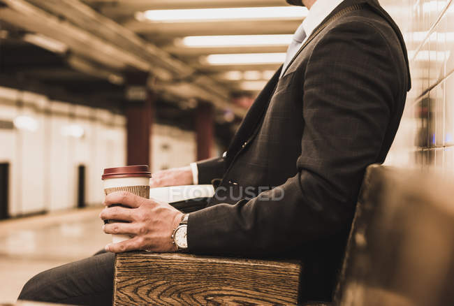 Junger Geschäftsmann wartet am U-Bahnsteig und hält Einwegbecher in der Hand — Stockfoto