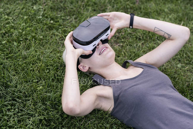 Mujer joven acostada en un prado con gafas de realidad virtual al aire libre - foto de stock