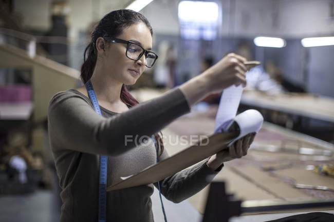 Designatore di moda nella fabbrica di abbigliamento che controlla il lavoro sugli appunti — Foto stock