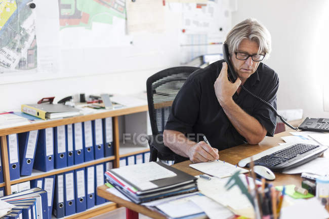 Hombre maduro telefoneando en el escritorio en la oficina - foto de stock