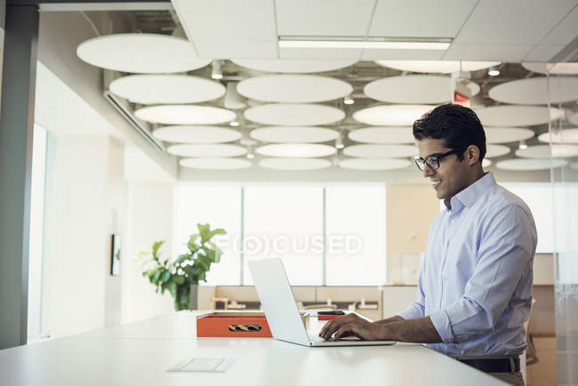 Businessman working at high desk with laptop in office — Stock Photo