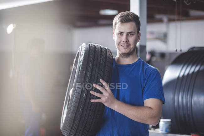 Junger Mechaniker mit Reifen in Werkstatt — Stockfoto